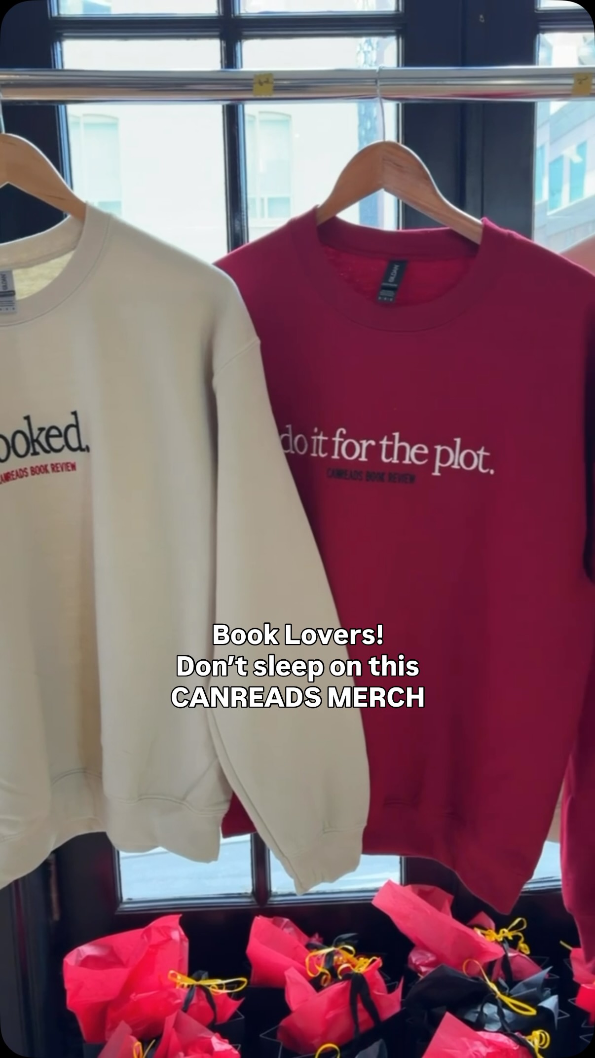 Cream and burgundy CANREADS sweatshirts on a display rail, including one that reads Do it for the plot.